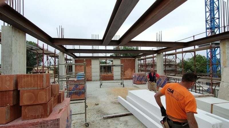 Cantiere di edificio in costruzione con travi in acciaio, pilastri in cemento armato e tamponamenti in laterizio.